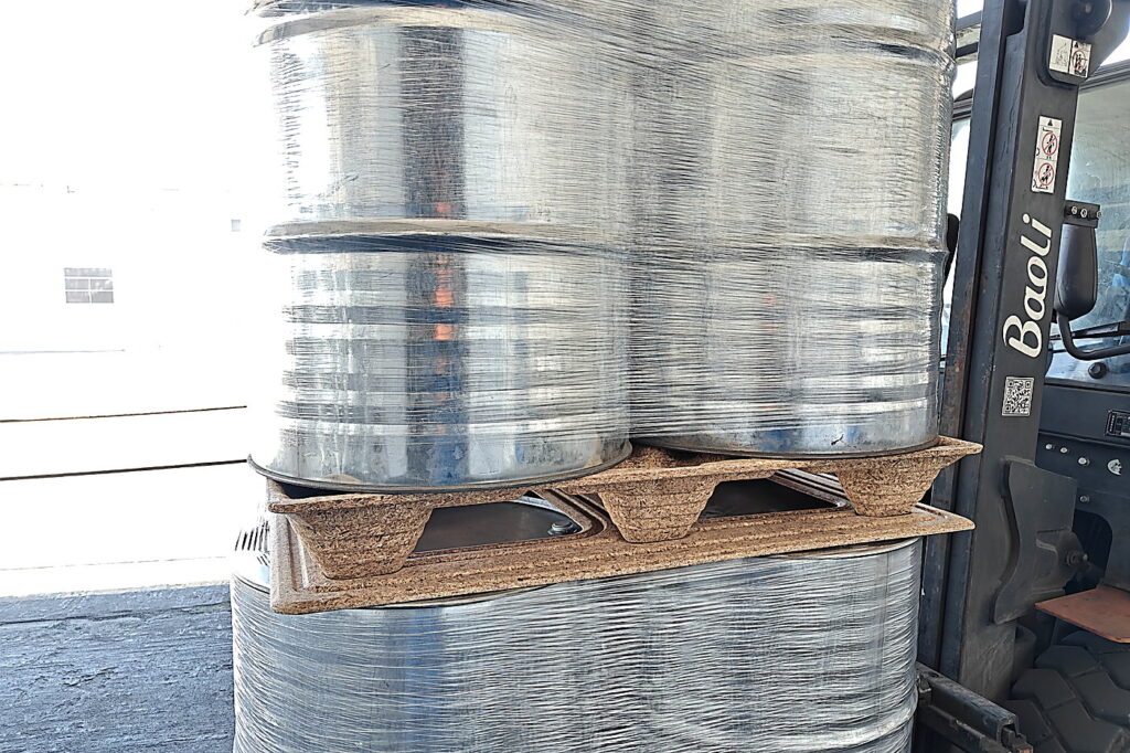 Forklift handling a molded wood pallet loaded with steel drums